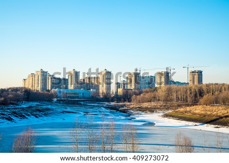 Residential buildings in winter with snow, park and city skyline with skyscrapers, blue sky.