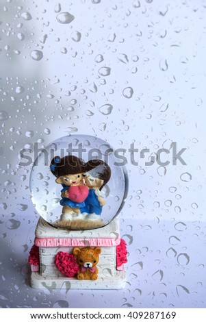 A lovely couple ceramic dolls in glass ball over natural rain drops background