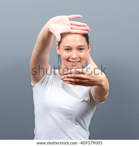 Portrait of a young woman making frame with hands against gray background