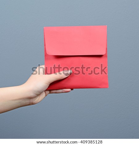 Hand holding red envelope against gray background