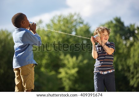 Two boys play tin can telephone with each other at the park Royalty-Free Stock Photo #409391674