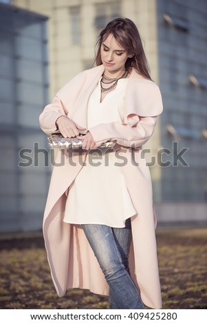 A woman in a pink coat holding handbag.