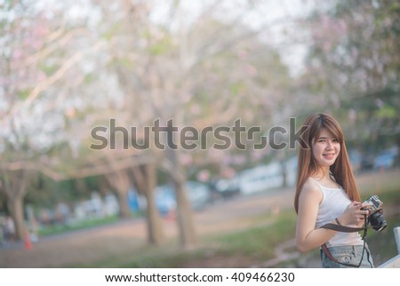 beautiful asian woman photographer holding camera seat Standing behind a tree with sunset time (selective focus)