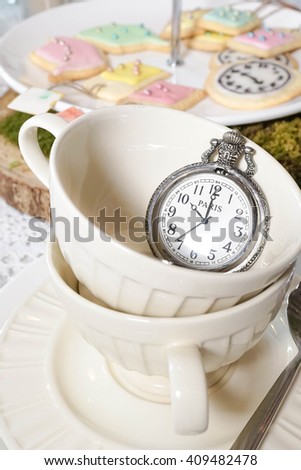 Close up porcelain teacup with pocket watch and colorful biscuits on the background, morning tea party 10 o'clock
