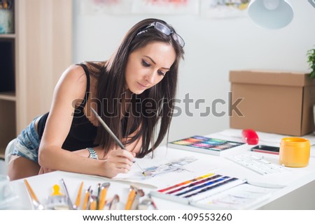 focused artist woman with long hair paints picture looking down