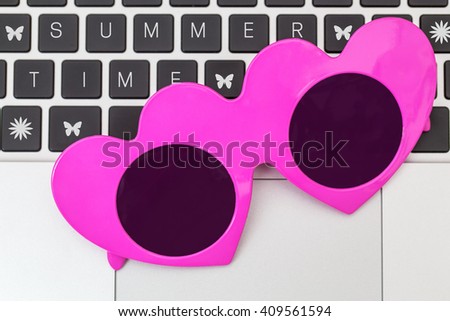 Pink heart shape sunglasses on laptop keyboard background with word SUMMERTIME, close up, top view. Summer time background in home office. Magnetic Magenta colored  sunglasses .