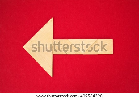 Flat lay - geometrical abstract background or arrow showing direction made of wooden tangram pieces. Unicolor background made of red fabric texture. Vignetting. 