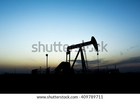 Sunset and silhouette of crude oil pumping unit in oilfield 