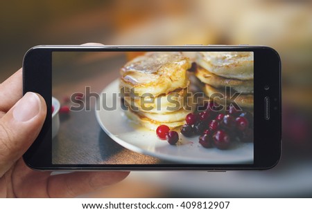 Taking picture of pancakes with mobile phone in female hands.Plate is on a wooden table. Vintage style.