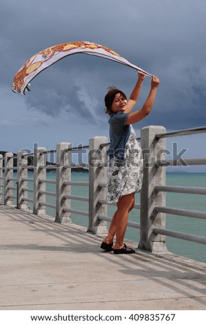 The woman holding white fabric at wind at the jetty.