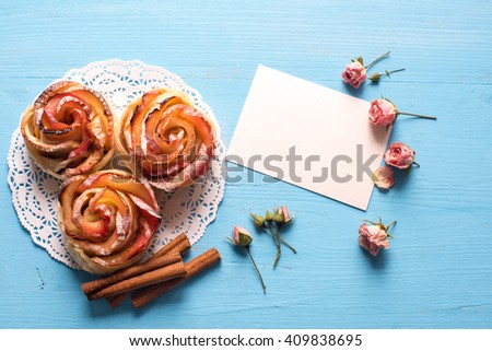 Homemade Apple rose cake with sugar powder on blue  wooden background.
Top view.  Handmade gift for mom/ Mothers day concept card.