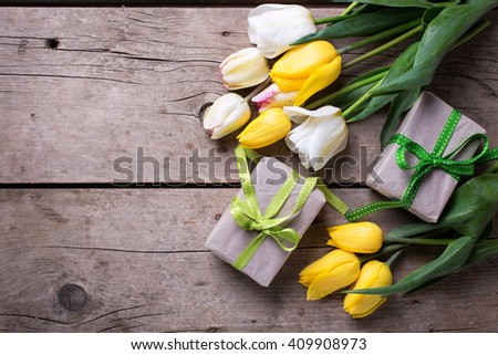 Bright yellow and white spring tulips and box with presents on vintage wooden background. Selective focus. Place for text.