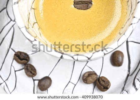 A shot of a coffee table book coffee beans and a creamy espresso in a white mug with black patterns