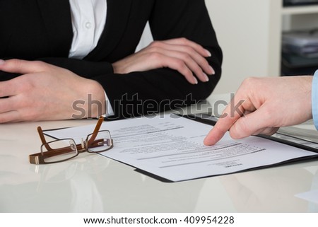 Close-up Of Businessperson Pointing On Document At Desk