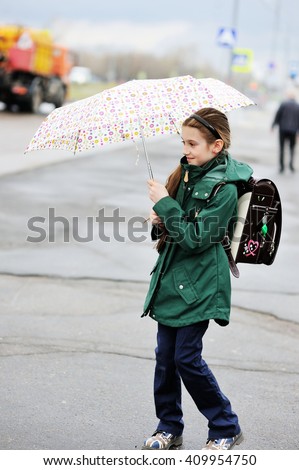 Adorable, elegant school aged kid  girl ,holding colorful umbrella walking in the city street in rainy day