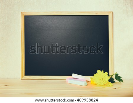 empty blank school black board with white chalks and chrysanthemum flower on wooden background, toned instagtam style, close up