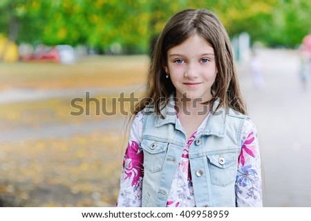 Adorable kid gir with long brunette hair playing in the sun in summer park