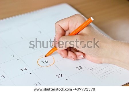 A female hand circling the date of the 15th day in the calendar Royalty-Free Stock Photo #409991398