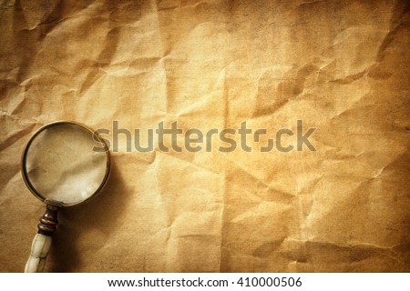 Vintage magnifying glass on old parchment paper background