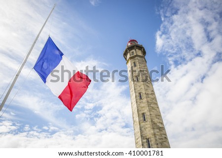 view from the ground of the 1854 Grand Phare des Baleines lighthouse with a French flag floating in front, Ile de Re, France.