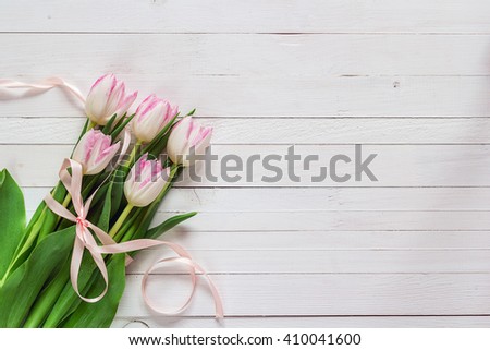 Bouquet of pink tulips with pink ribbon on white painted wooden background and empty space for text. Top view with copy space