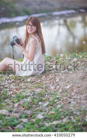 Woman wearing glasses holding a camera, sitting under a tree next dive.