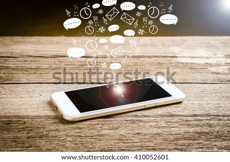 White smart phone on a wooden table emitting holographic image of social media related icons. 