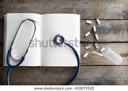 Stethoscope with open book and pills on wooden background. Medical literature concept