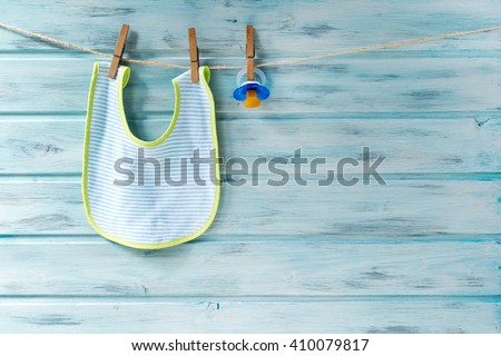 Baby bib and pacifier hanging on a clothesline on wooden background Royalty-Free Stock Photo #410079817