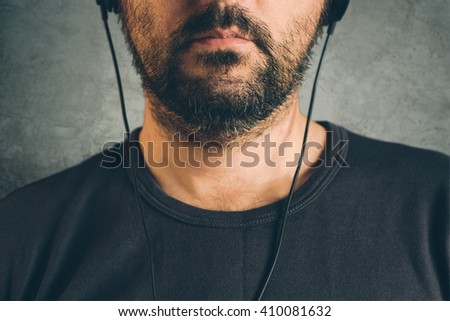 Unshaven adult man listening to music on headphones, enjoy favourite song, half face low key portrait