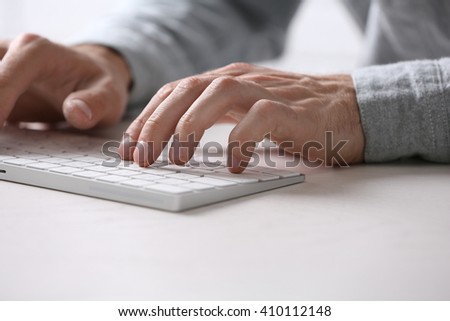 Male hands typing on wireless keyboard at table closeup
