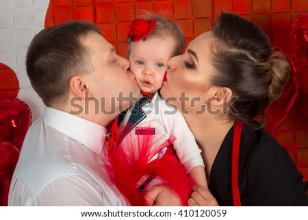 Father and mother are kissing their little daughter