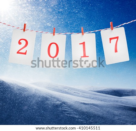 Paper or photo frames with 2017 numbers hanging on the red striped rope. Snowstorm in sunny day background. New year design