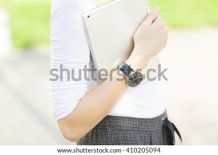 Close-up of female arm wearing a watch and carrying a digital tablet outdoors.