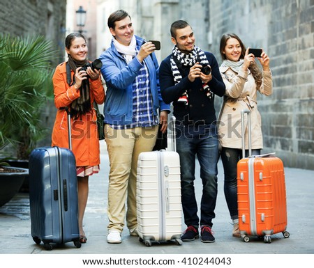 Group of positive young tourists walking through street with camera and smartphone