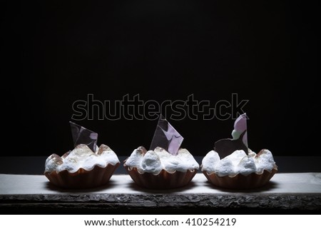 Tartlets with white cream and chocolate on the board on a dark background. Toned.