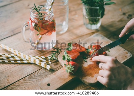 Making of lemonade or cocktail with strawberry and rosemary on wooden table. Toned picture