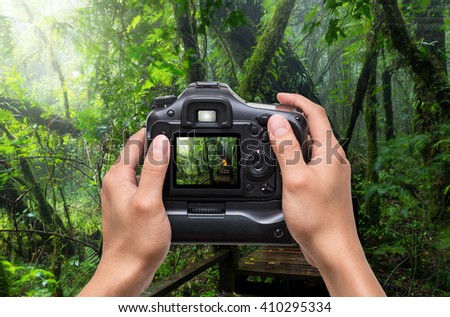Hands holding the camera which taking photo of Traveller taking photo at Beautiful rain forest at ang ka nature trail in doi inthanon national park, Thailand