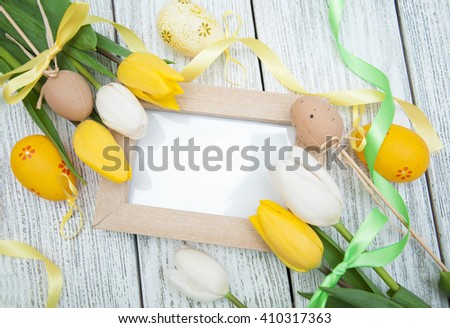 Tulips, blank picture frame, easter eqqs and ribbon on a white wooden background. Top view with copy space
