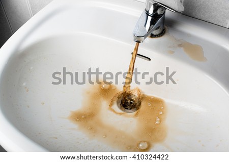 Dirty brown water running into a white sink. Looks very unhealthy, Royalty-Free Stock Photo #410324422