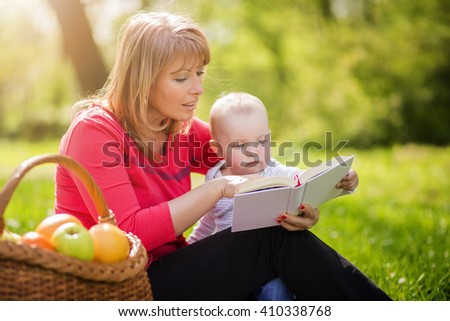 Picture of mature woman with son sitting down on green grass field and read fairytale in park
