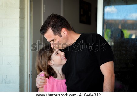 A father kisses his daughter on the forehead as he hugs her and pulls her close.