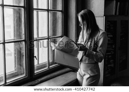 Beautiful stylish young  girl reading a book near the vintage  window in library. Black and white photo