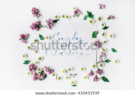 inspirational quote "everyday is a new adventure" written in calligraphy style on paper with wreath frame with lilac and chamomile isolated on white background. flat lay, overhead view, top view
