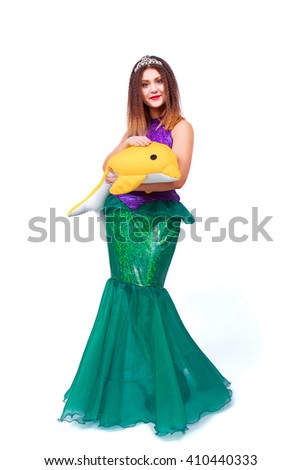 Beautiful girl posing in fantasy mermaid costume with toy dolphin, isolated on a white background