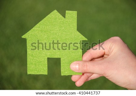 Hand holding eco house icon concept on the green grass background 