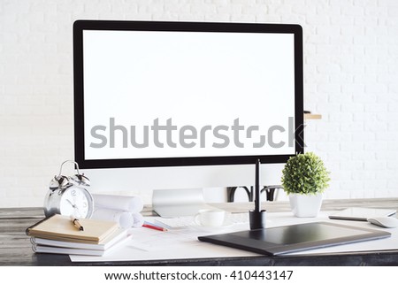 Designer desktop with blank white computer screen, graphic tablet, alarm clock and other items. White brick background. Mock up