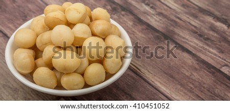 Peeled macadamia nut in white bowl over wooden background