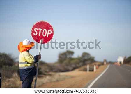 The worker construction hand hold circle red road stop sign held at side country highway road landscape in Australia road maintenance Vintage Tone. Careful Keep slow down Traffic control. Man. 