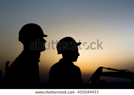 Silhouette of construction workers at construction site in oilfield - Blur background with heavy lifting equipment - Sunset.    Royalty-Free Stock Photo #410544415